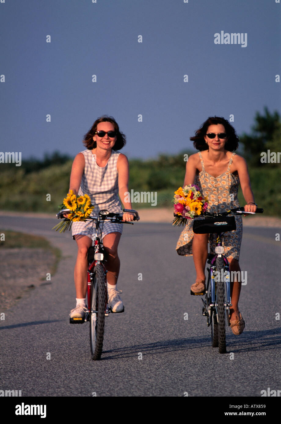 Zwei junge 25 auf 30 bis 35 Jahre alten Frauen sitzen auf dem Fahrrad mit Korb mit Blumen, Southampton, Long Island, New York State, USA Stockfoto