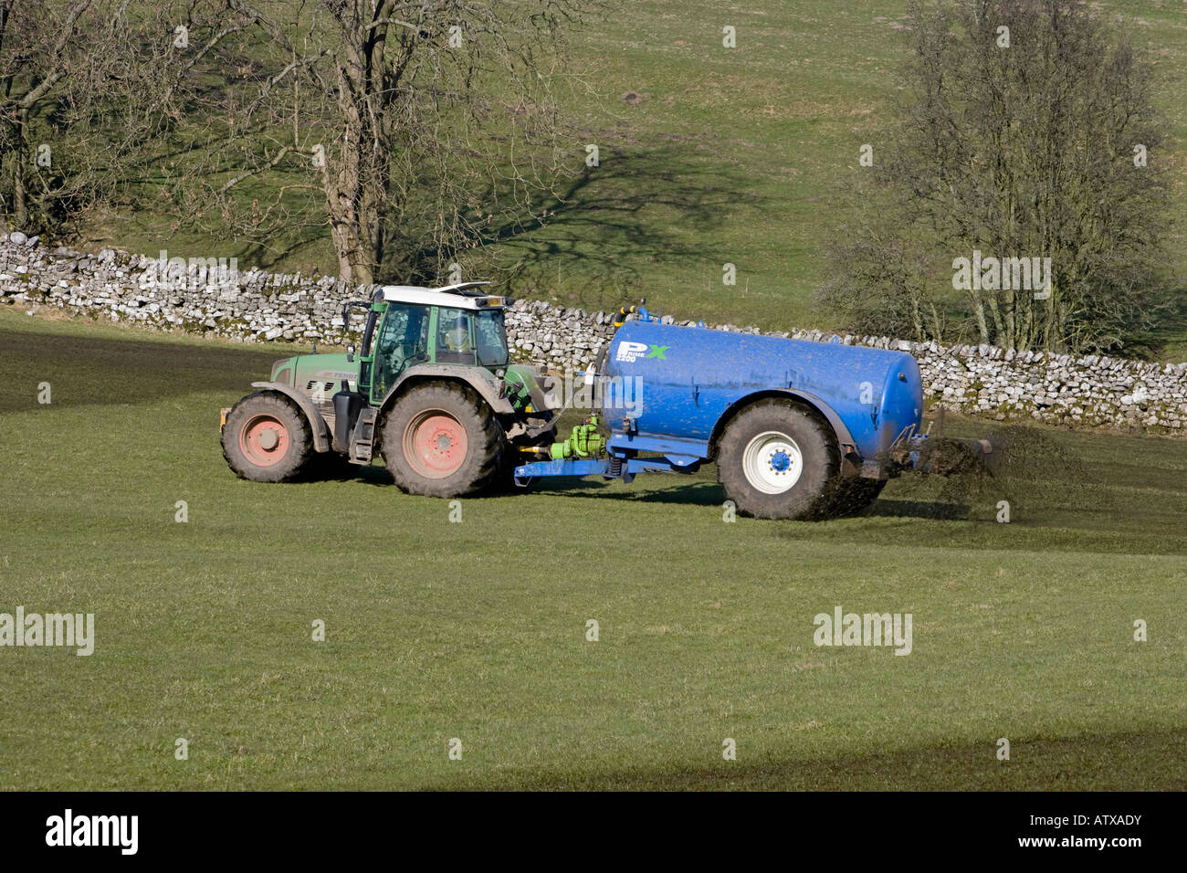 Landwirt arbeiten Fahren grünen Traktor & zylindrischen Düngertank Sprühen Entlammung auf Ackerland Weidefeld Gras - Yorkshire, England Großbritannien Stockfoto