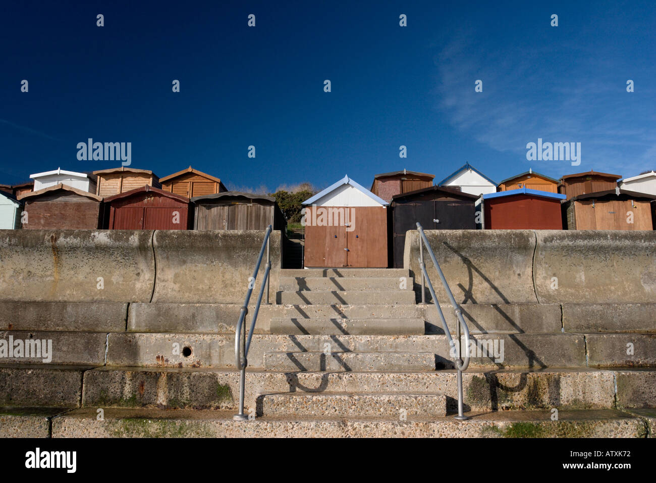 Frinton am Meer Strandhütten hinter der gekrümmten Beton Ufermauer vor blauem Himmel Stockfoto