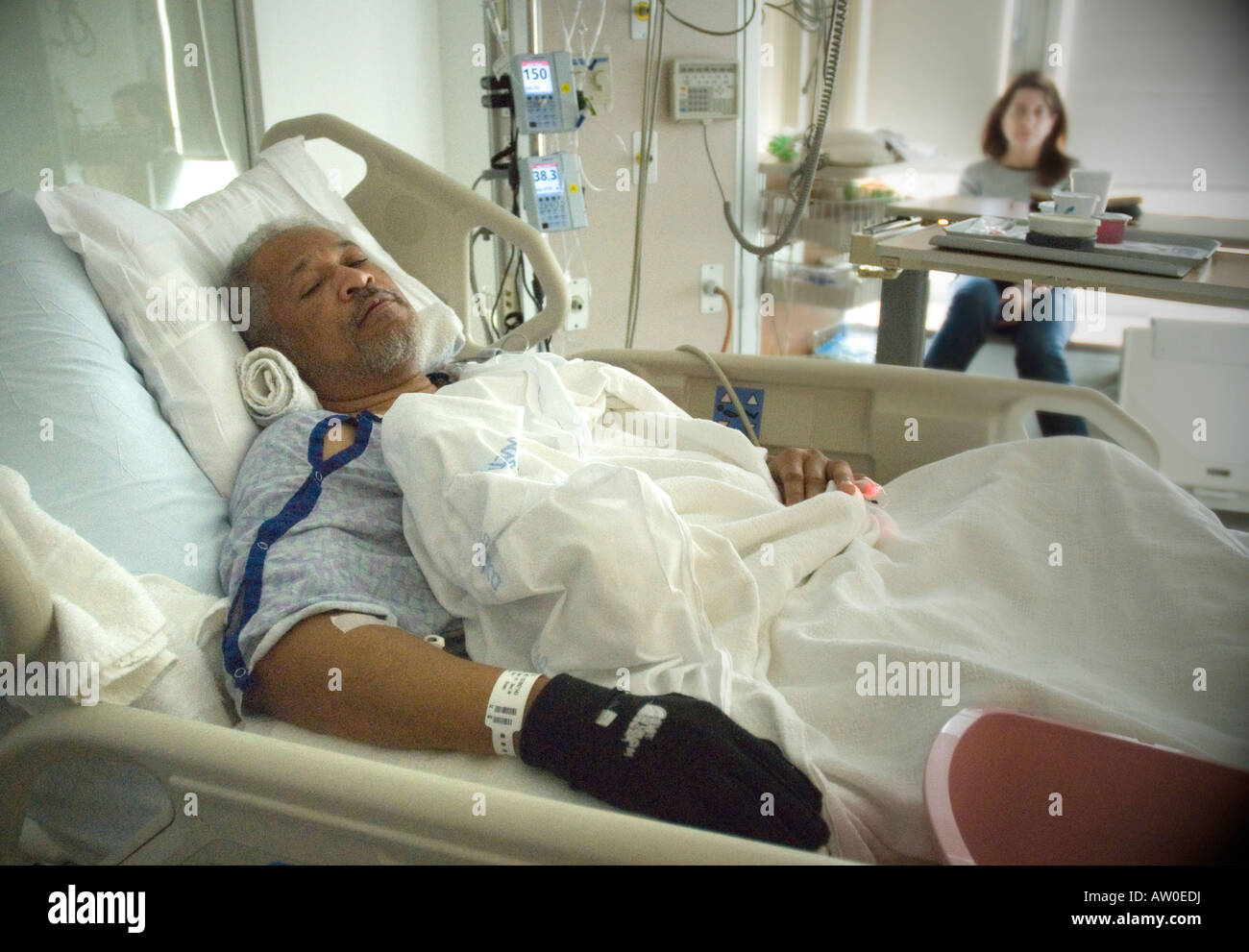 Einen schwarzen Mann liegt in einem Krankenhaus Intensivstation (ICU) erholt sich wie eine betroffene Frau im Hintergrund blickt auf. Stockfoto
