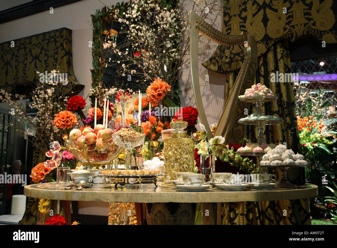 Spitze der Oval geformte Marmortisch inmitten antiker Behälter für den High Tea. Wand hinter hat eine riesige Palette von Blumenarrangements. Stockfoto