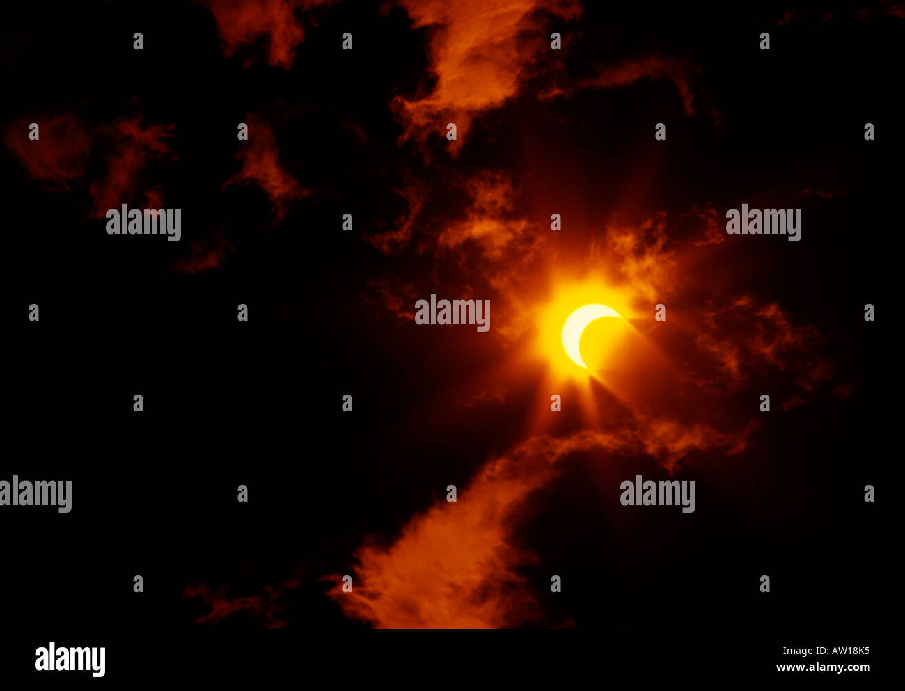 Eine partielle Sonnenfinsternis wird durch Wolken erfasst, die in roten und Orangen beleuchtet sind. Die Sonne nimmt einem Halbmond. Stockfoto