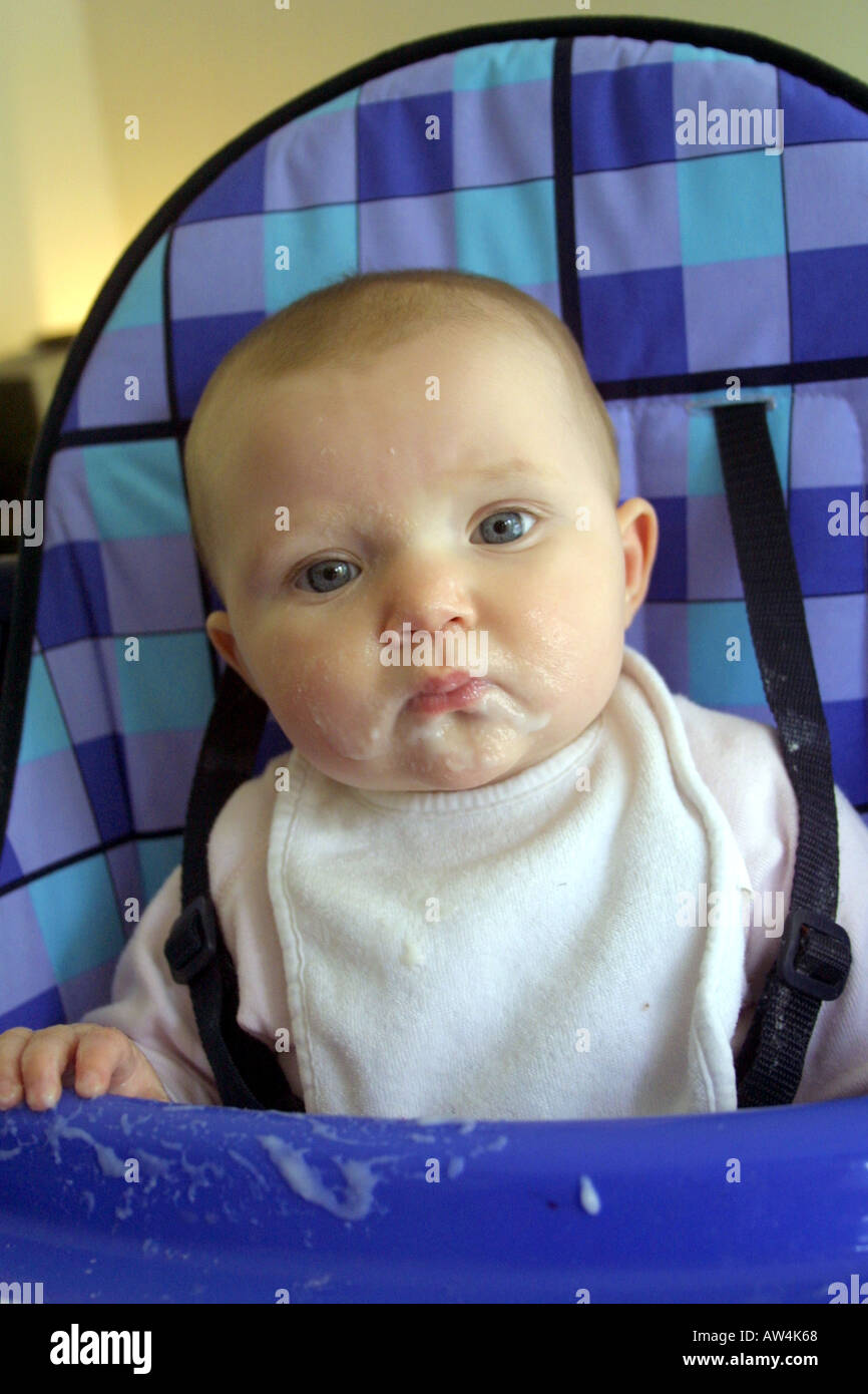 Fünf Monate altes Baby im Hochstuhl wird Löffel gefüttert mit Gesicht voller Joghurt Stockfoto