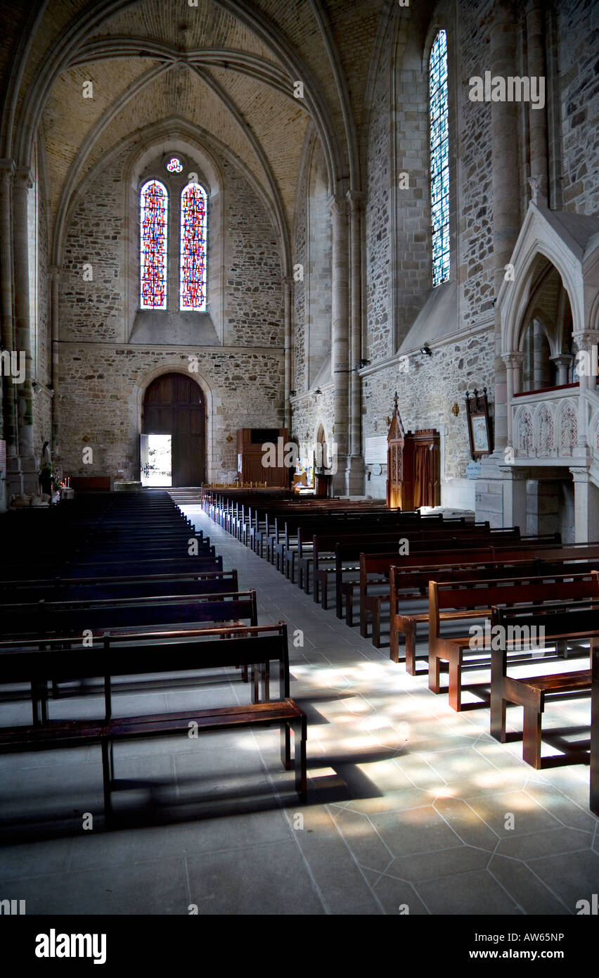 Innenansicht des Abbaye de Lehon Brittany mit einem Buntglasfenster, Kirchenbänken, der Kanzel und einem durch ein anderes Fenster strahlenden Licht Stockfoto