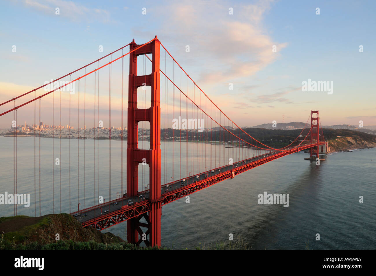 Golden Gate Bridge von der untergehenden Sonne vor dem Hintergrund der Skyline von San Francisco und schönen bewölkten Himmel beleuchtet Stockfoto