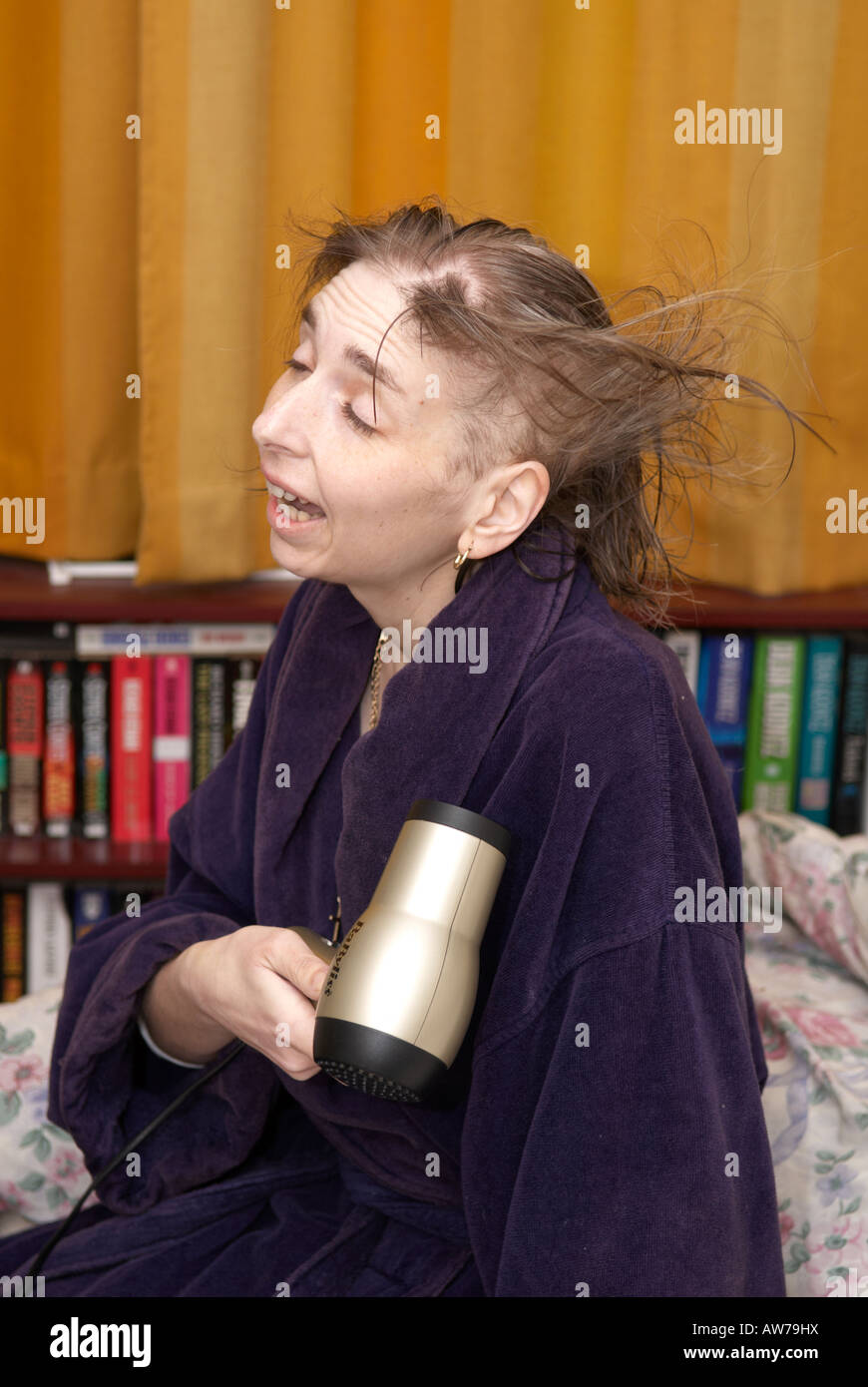 Lady amüsiert sich in ihrem Schlafzimmer Föhnen ihre Haare die aufgrund von Chemotherapie Ausdünnung Stockfoto
