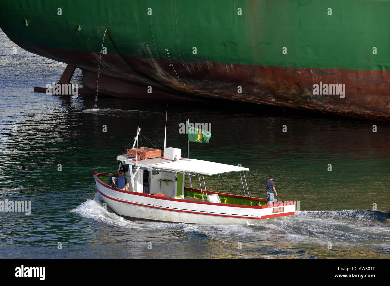 Ein kleines Fischerboot geht ein großes Containerschiff an einem schönen sonnigen Morgen im Hafen von Fremantle, Perth, Western Australia Stockfoto