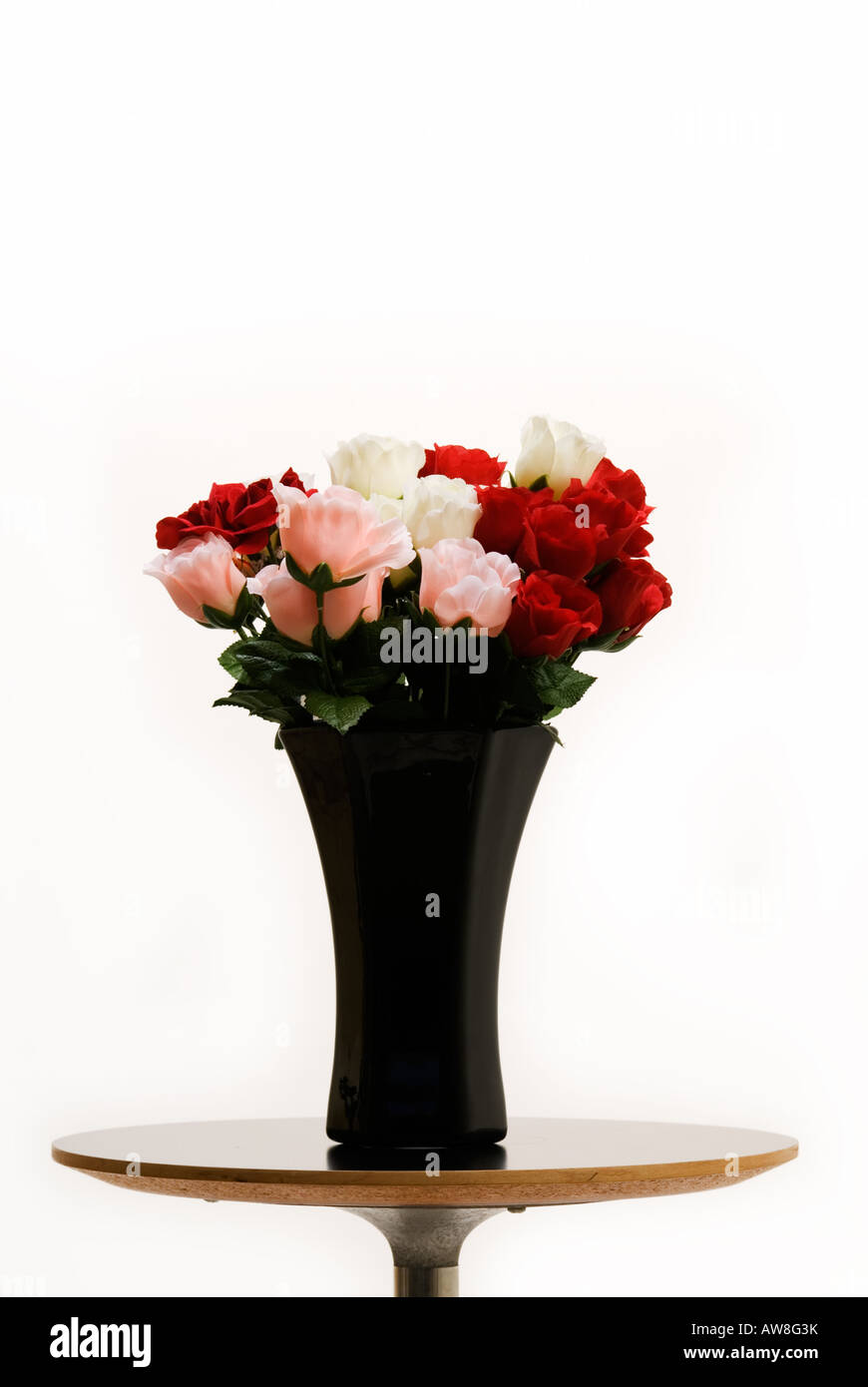 Kleiner Beistelltisch mit einer schwarzen Vase voller rote und rosa Rosen auf einem farbigen Hintergrund isoliert Stockfoto