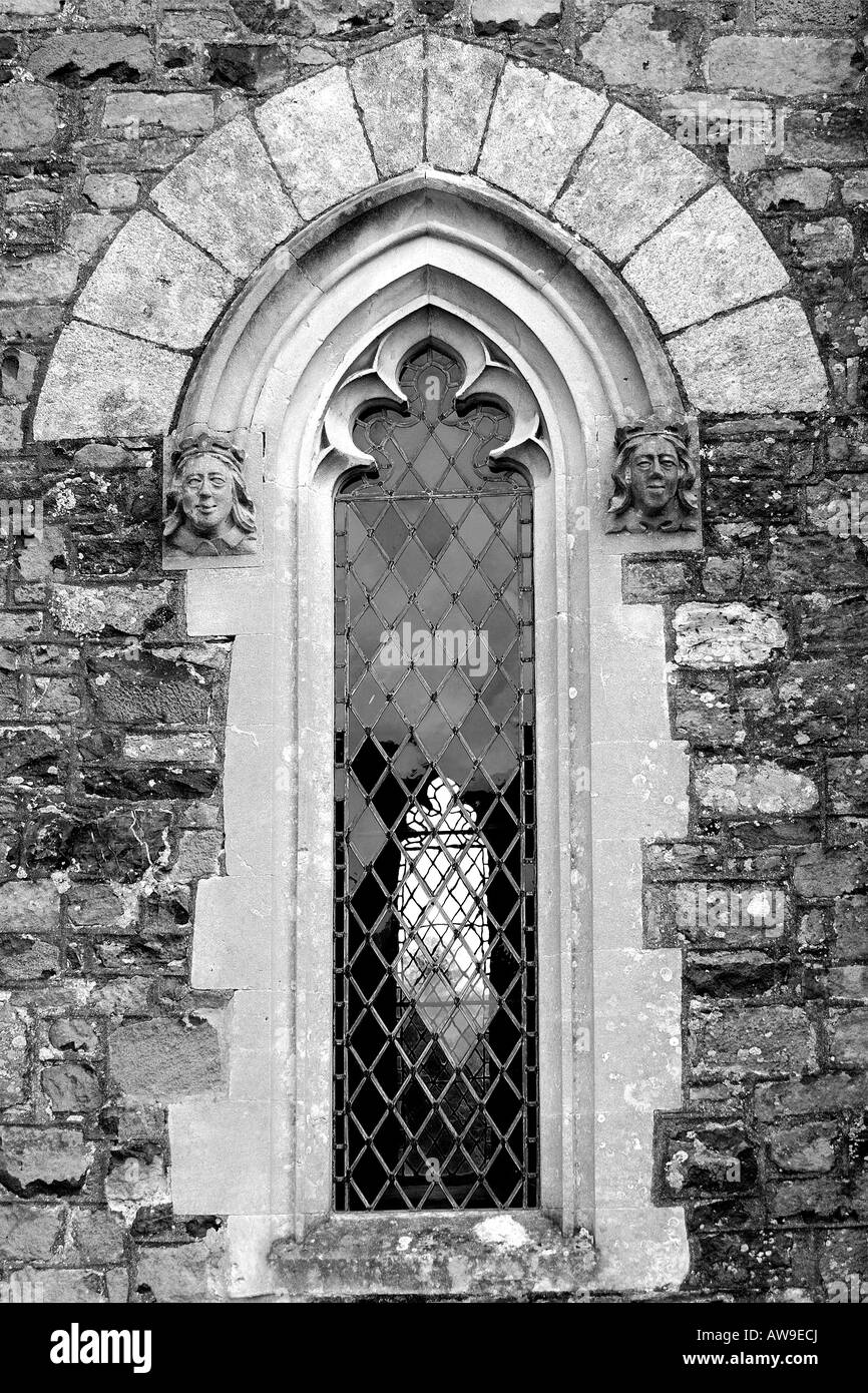 Architektonisches Detail nahe, von einem gotischen gewölbt Kirchenfenster mit steinernen Gesichtern jeder Seite und klar verbleites Glas in Monochrom Stockfoto