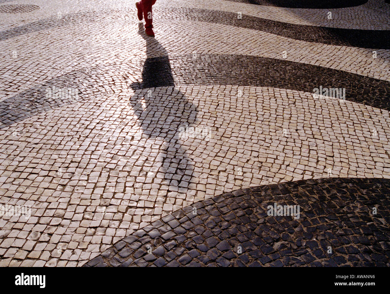 A mans Füße und langen Schatten zu Fuß über ein Mosaik Street, Largo de Santo Agostinho, Macau. Stockfoto