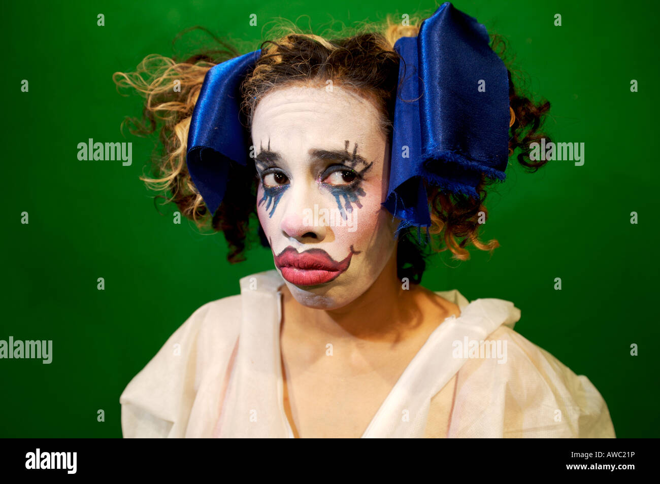 junge Frau im gotischen Puppe/Clown Make-up mit blauen Schleifen im Haar sieht traurig Stockfoto