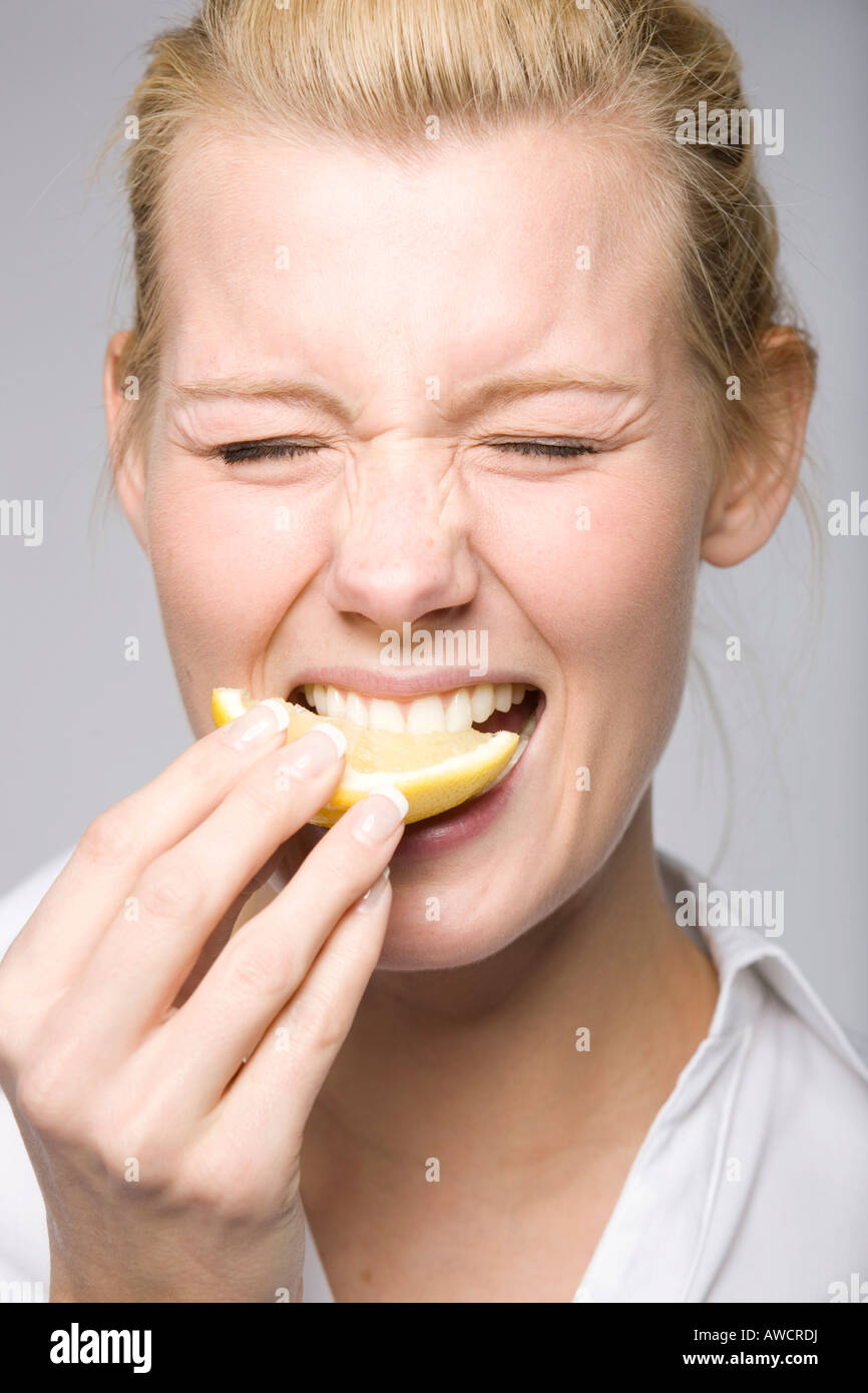 Junge Frau in eine Zitrone beißt und machen ein lustiges Gesicht Stockfoto