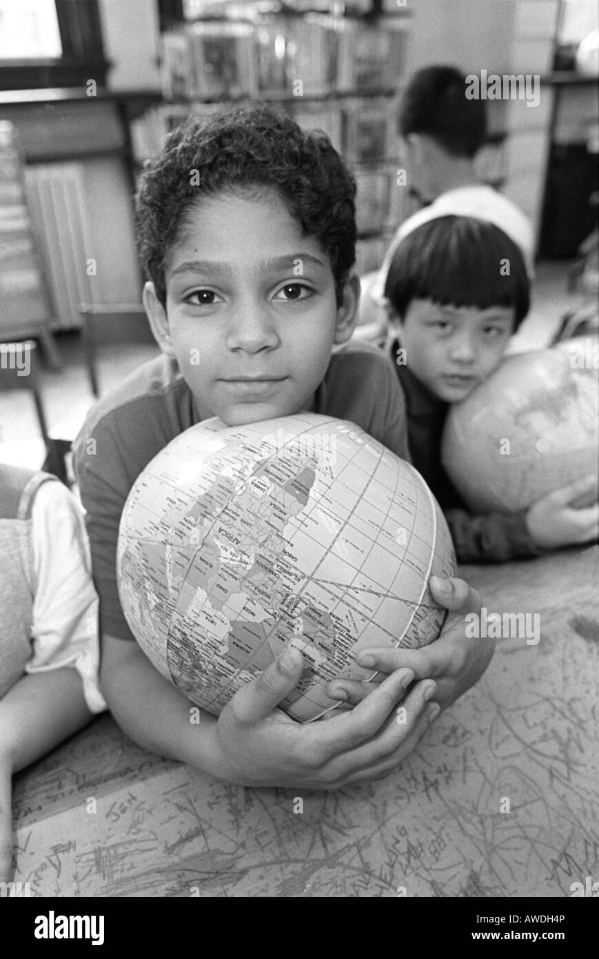 Grundschule Kind mit der Welt in seinen Armen während einer Geographie-Klasse in der Bibliothek in New York City Stockfoto