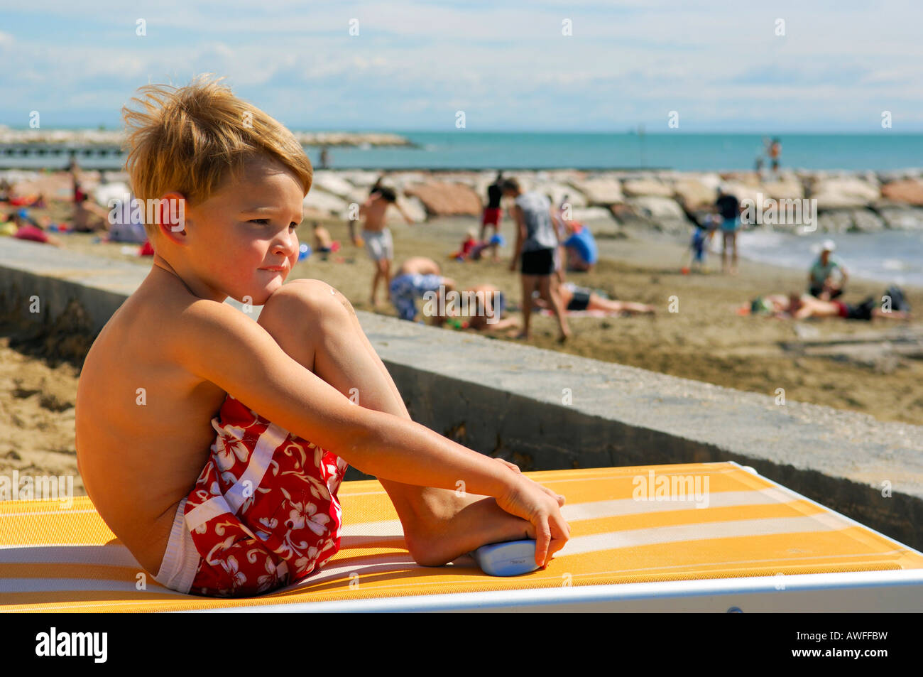 Junge sitzt auf einer Liege am Strand, Caorle, Venetien, Italien Stockfoto