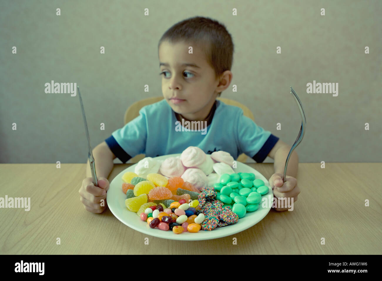 Kleiner Junge mit Messer und Gabel befasst sich mit einem Teller voller Süßigkeiten, die aussehen wie eine Mahlzeit Stockfoto