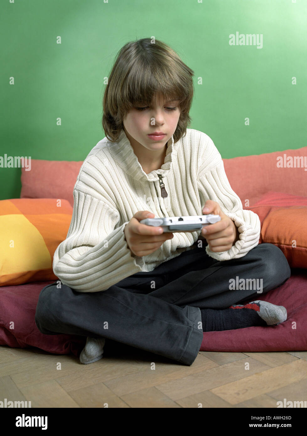 kleiner Junge Schneidersitz sitzen und mit Gameboy spielen Stockfoto