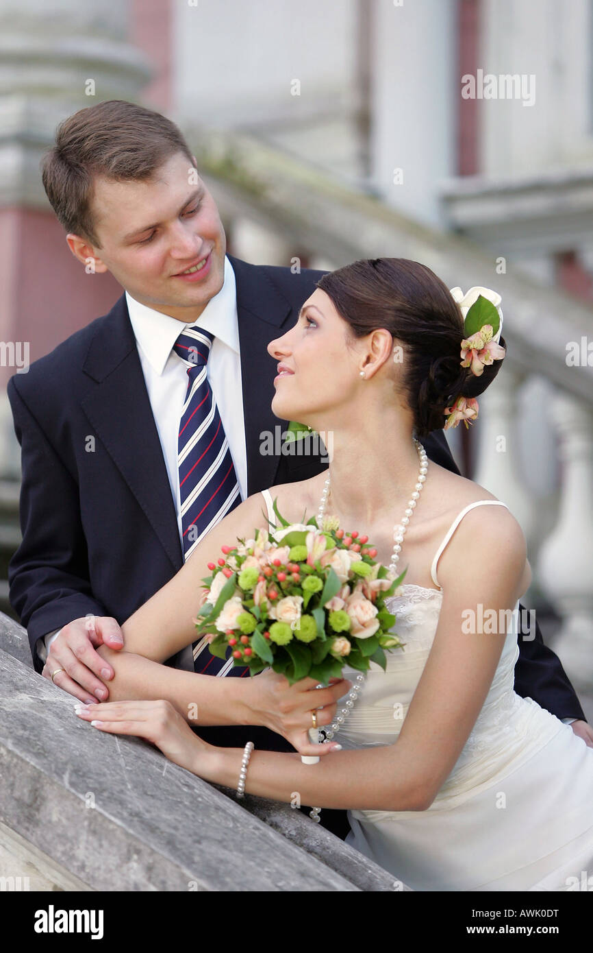 Schöne lächelnde Braut im weißen Kleid am Hochzeitstag. Sie hält einen Blumenstrauß und liebevoll mit Blick auf den Bräutigam Stockfoto
