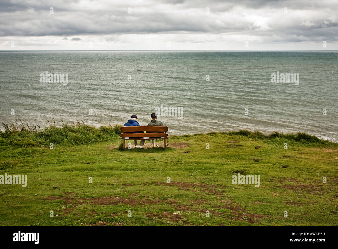 Älteres paar sitzen auf Holzbank Blick auf das Meer im Herbst / Winter Stockfoto