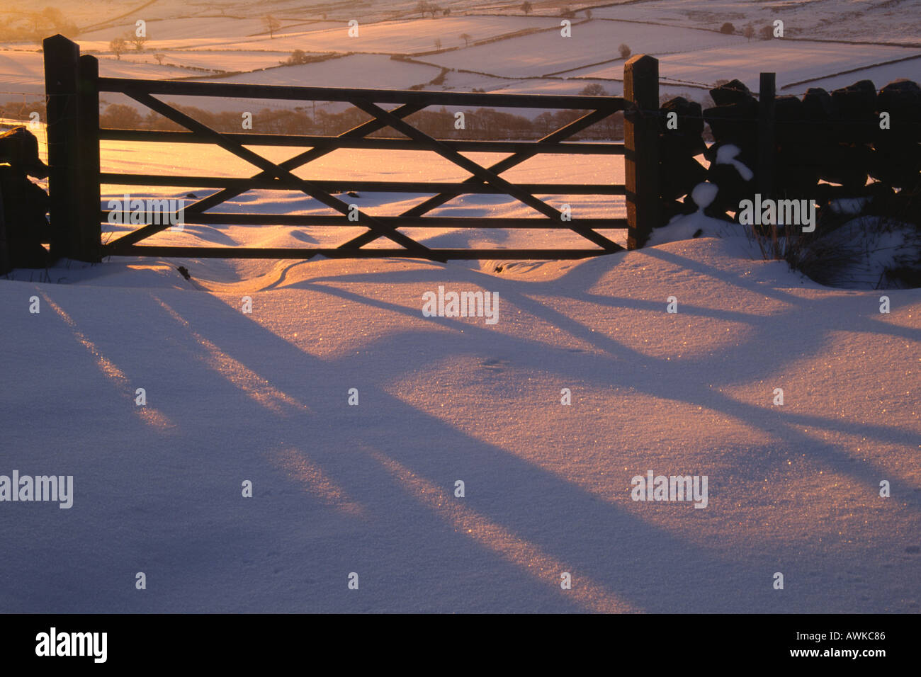 Holztor inmitten einer Trockensteinmauer Hintergrundbeleuchtung mit Schatten fallen auf Schnee Stockfoto