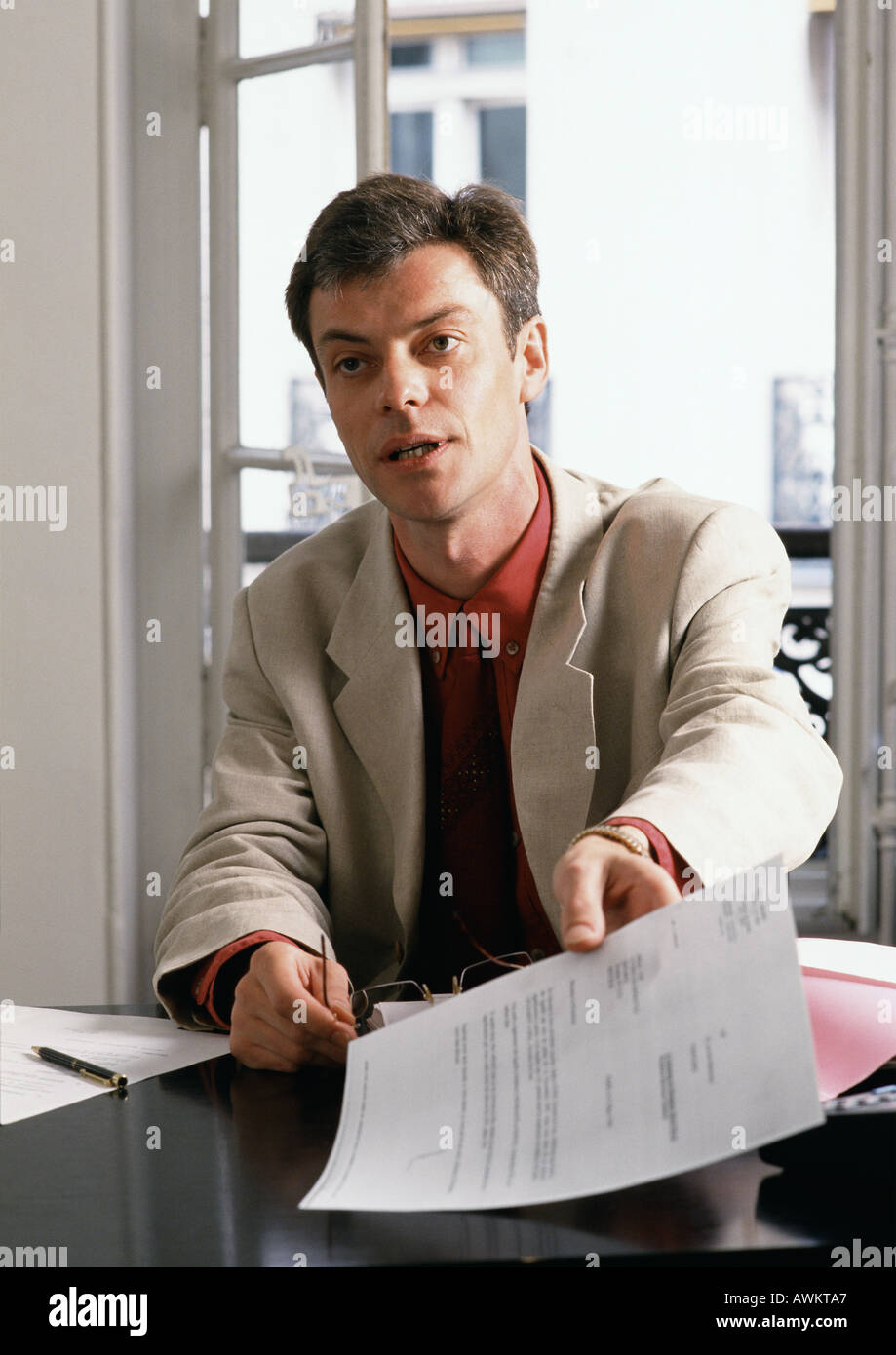 Mann am Schreibtisch sitzt, hält Dokument Stockfoto