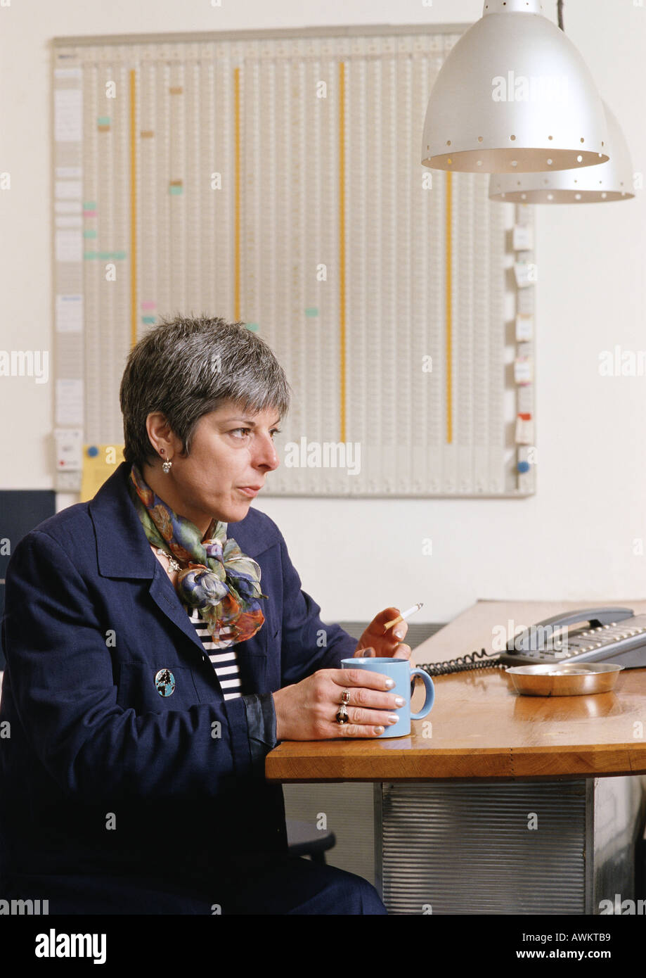 Frau sitzt am Tisch, mit Cup und qualmender Zigarette Stockfoto