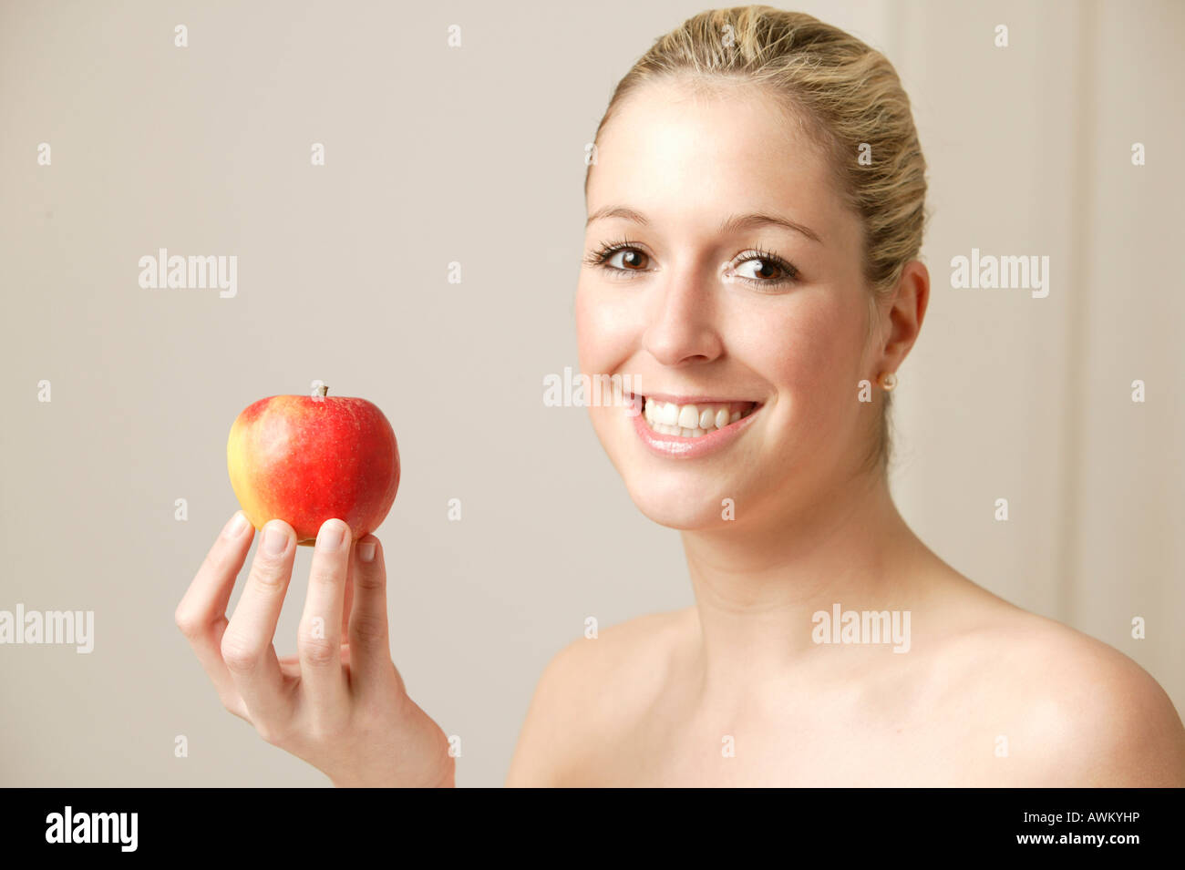 Lächelnde junge blonde Frau hält einen Apfel Stockfoto