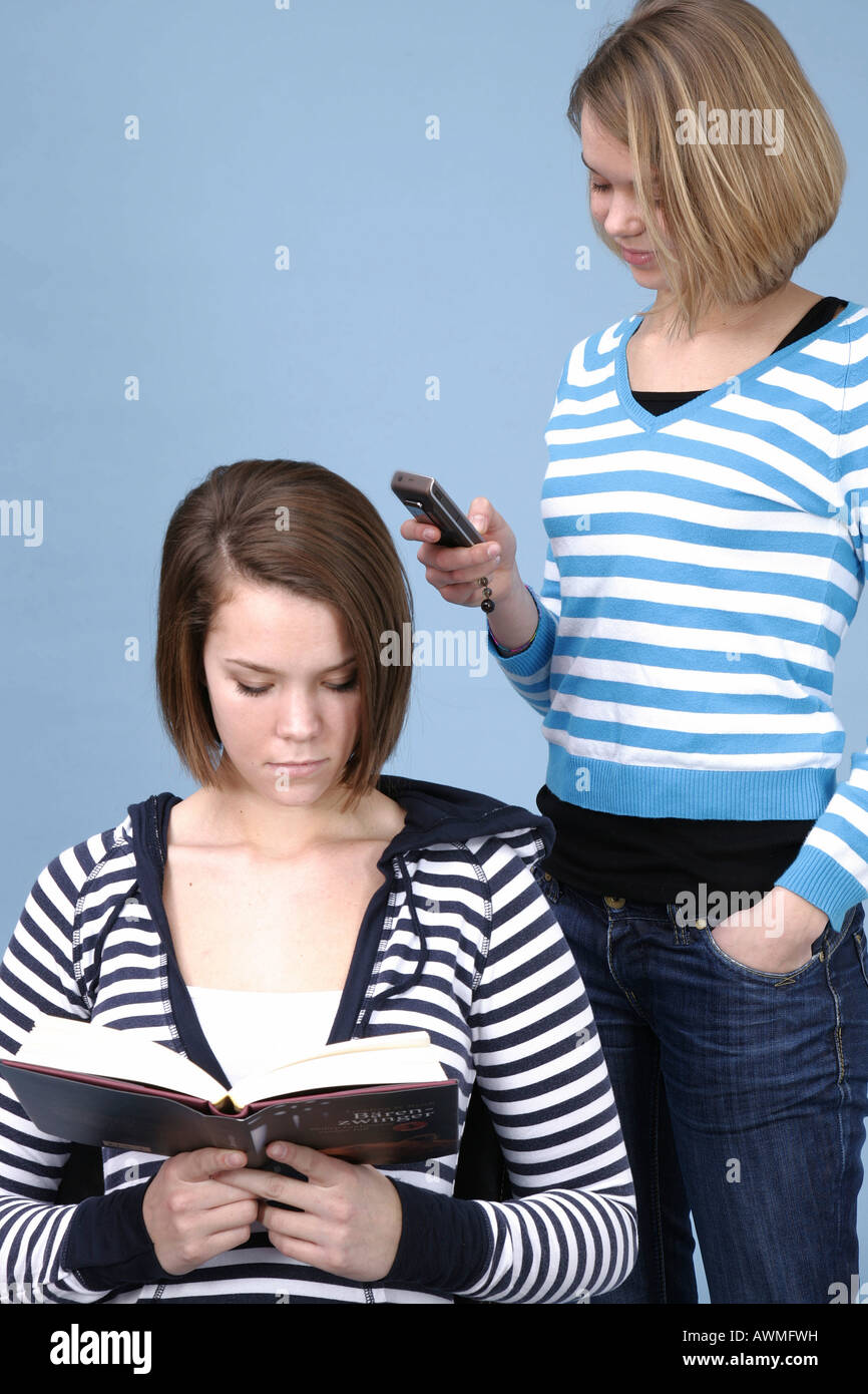 Zwei Mädchen, einer Lesung, die andere beschäftigt mit ihrem Handy, Handy Stockfoto