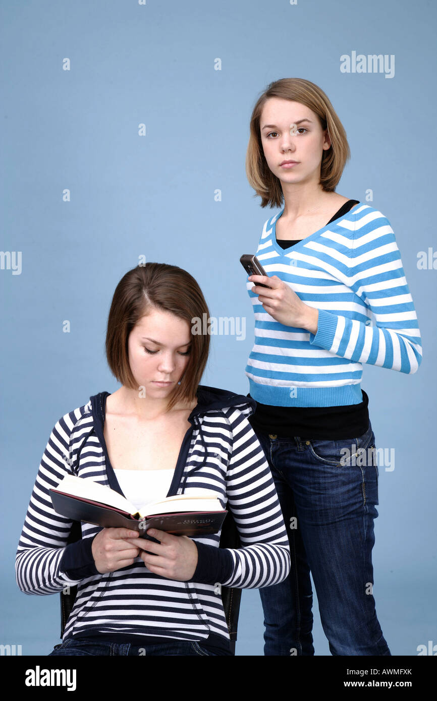 Zwei Mädchen, einer Lesung, die andere beschäftigt mit ihrem Handy, Handy Stockfoto