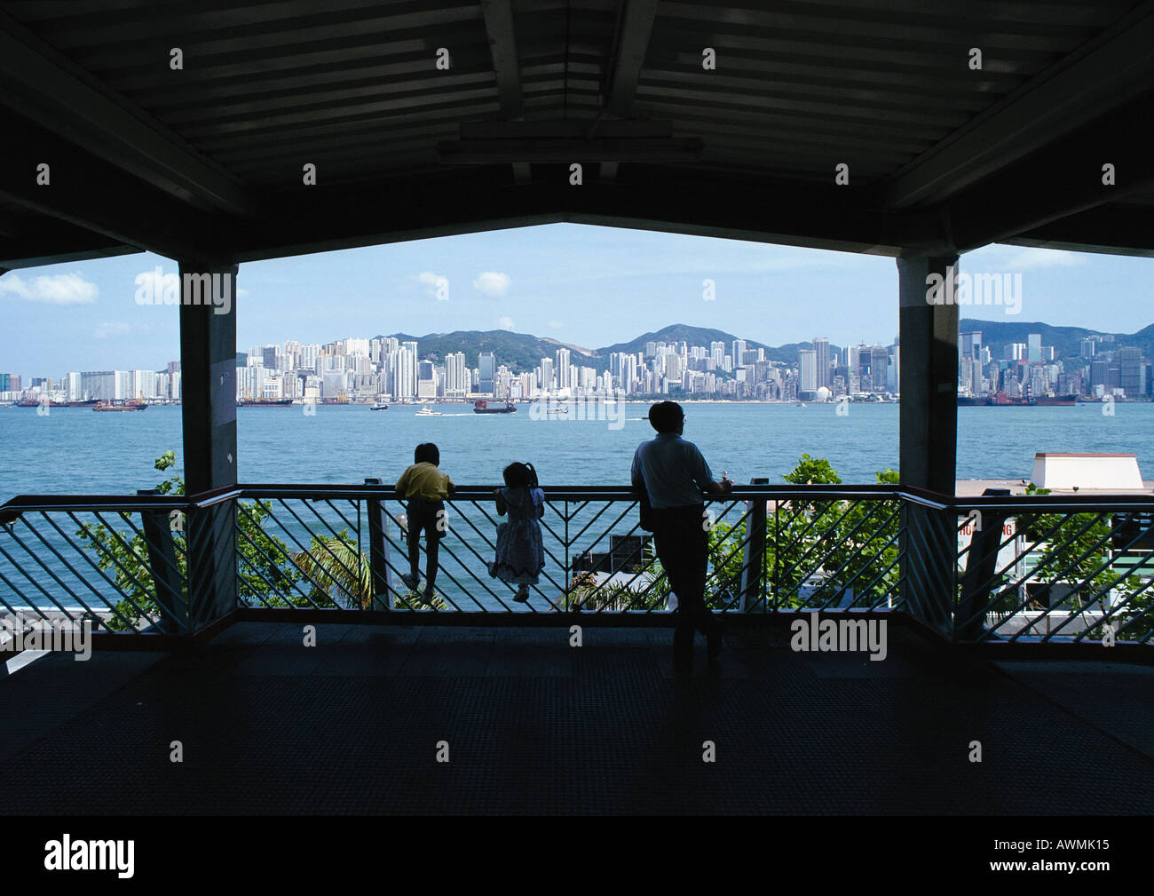 Hong Kong, Silhouetten von Erwachsenen mit zwei Kindern stützte sich auf Schiene, Rückansicht, Stadt in Ferne Stockfoto