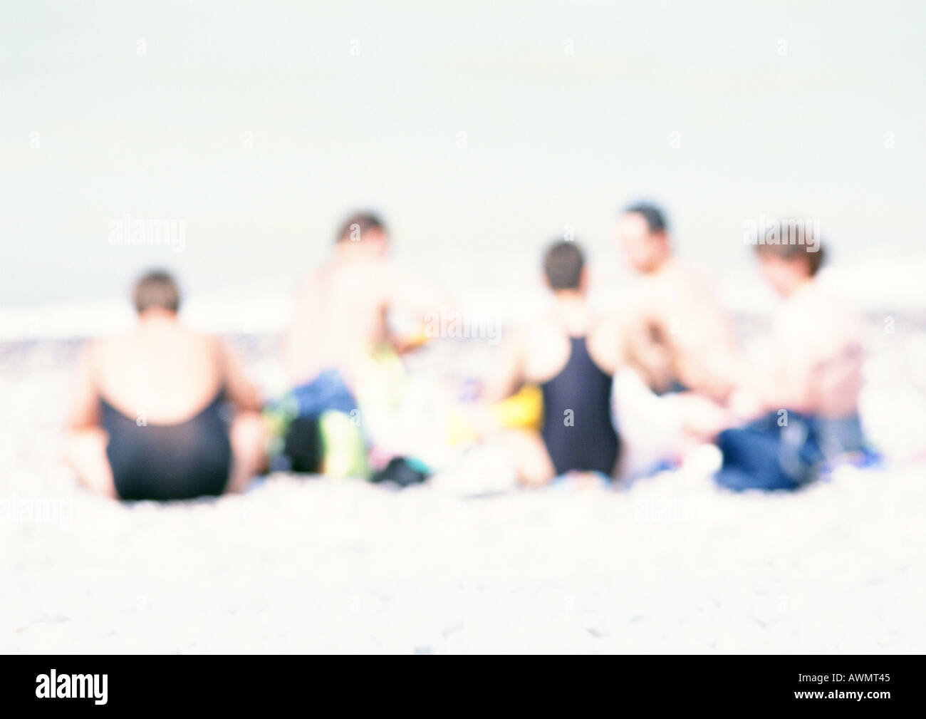 Gruppe von Menschen sitzen auf Sand am Strand, unscharf Stockfoto