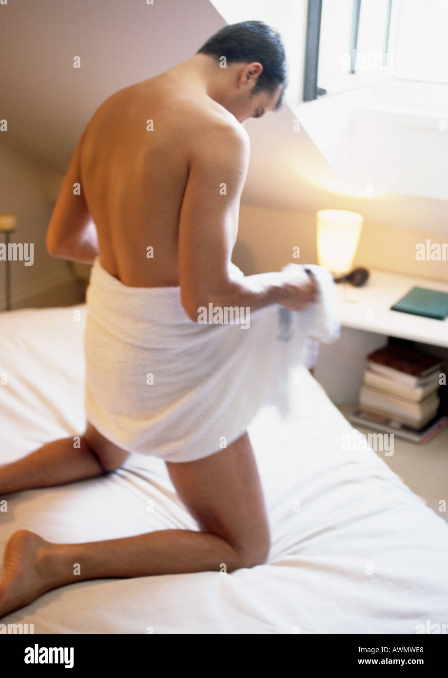 Mann kniet auf Bett, Holding Handtuch öffnen um Taille, Blick nach unten, in vollen Länge. Stockfoto