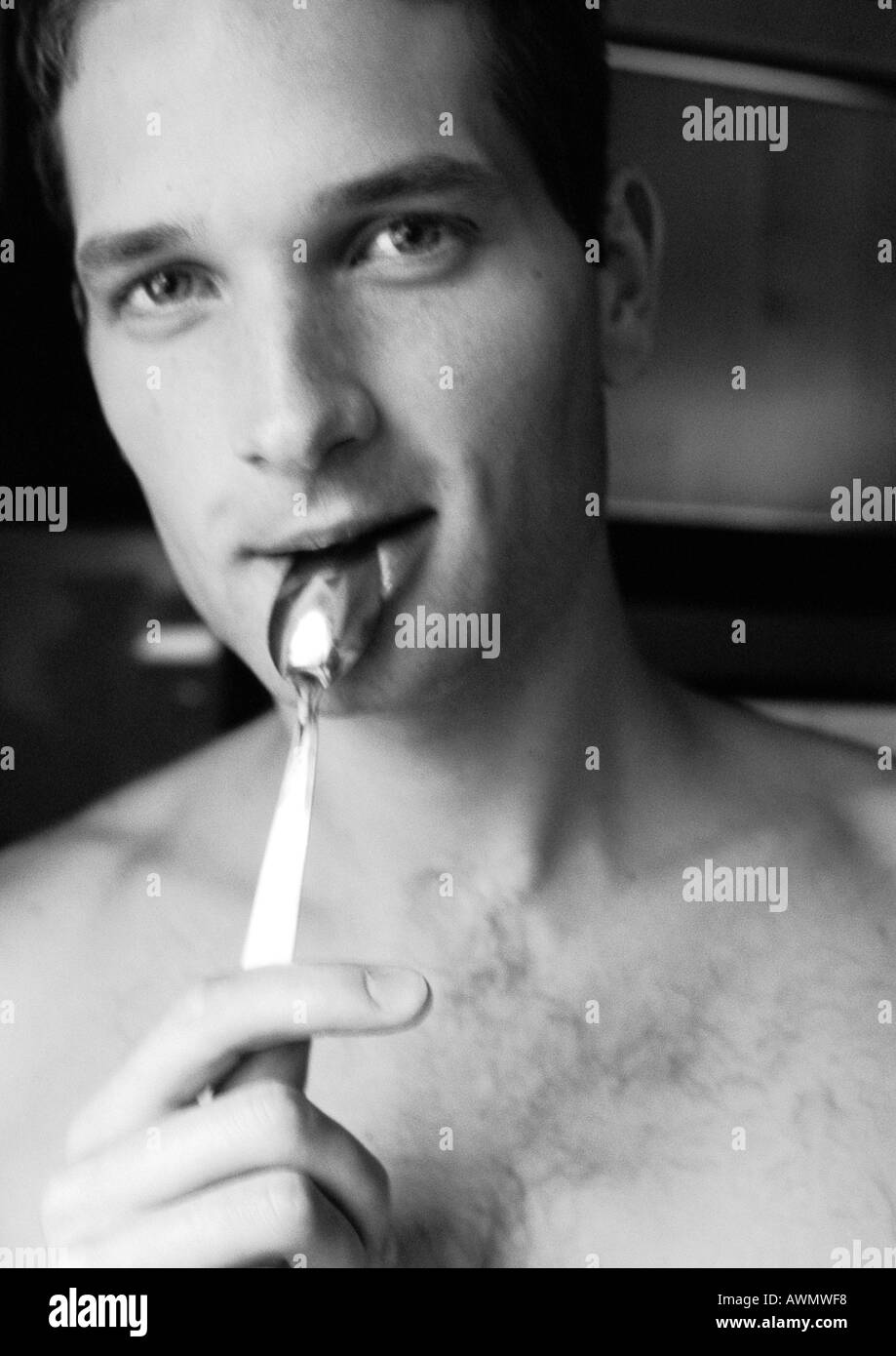 Drilliche Mann, der Löffel an Lippen, Blick in die Kamera, close-up, schwarz und weiß. Stockfoto
