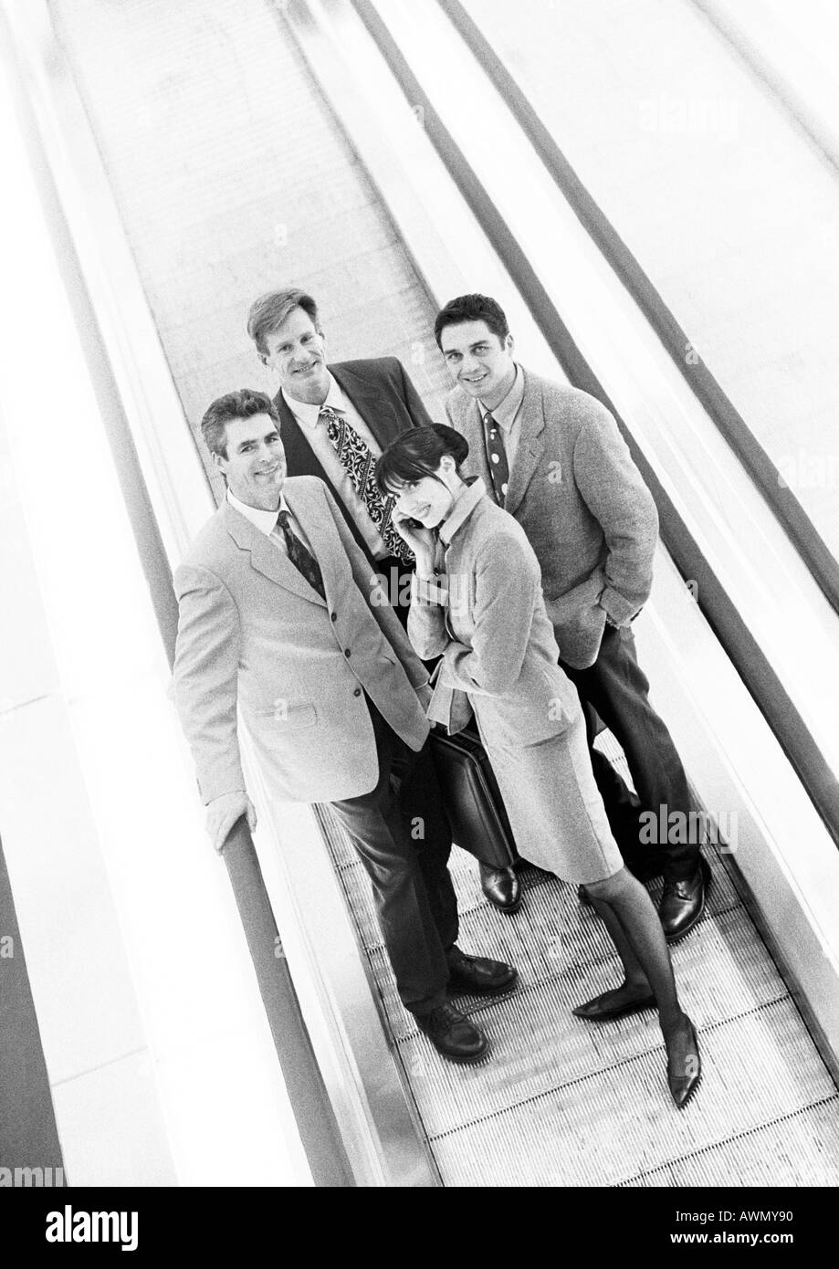 Gruppe von Geschäftsleuten auf Laufband lächelnd in die Kamera, Business-Frau vorne auf Handy, b&w. Stockfoto