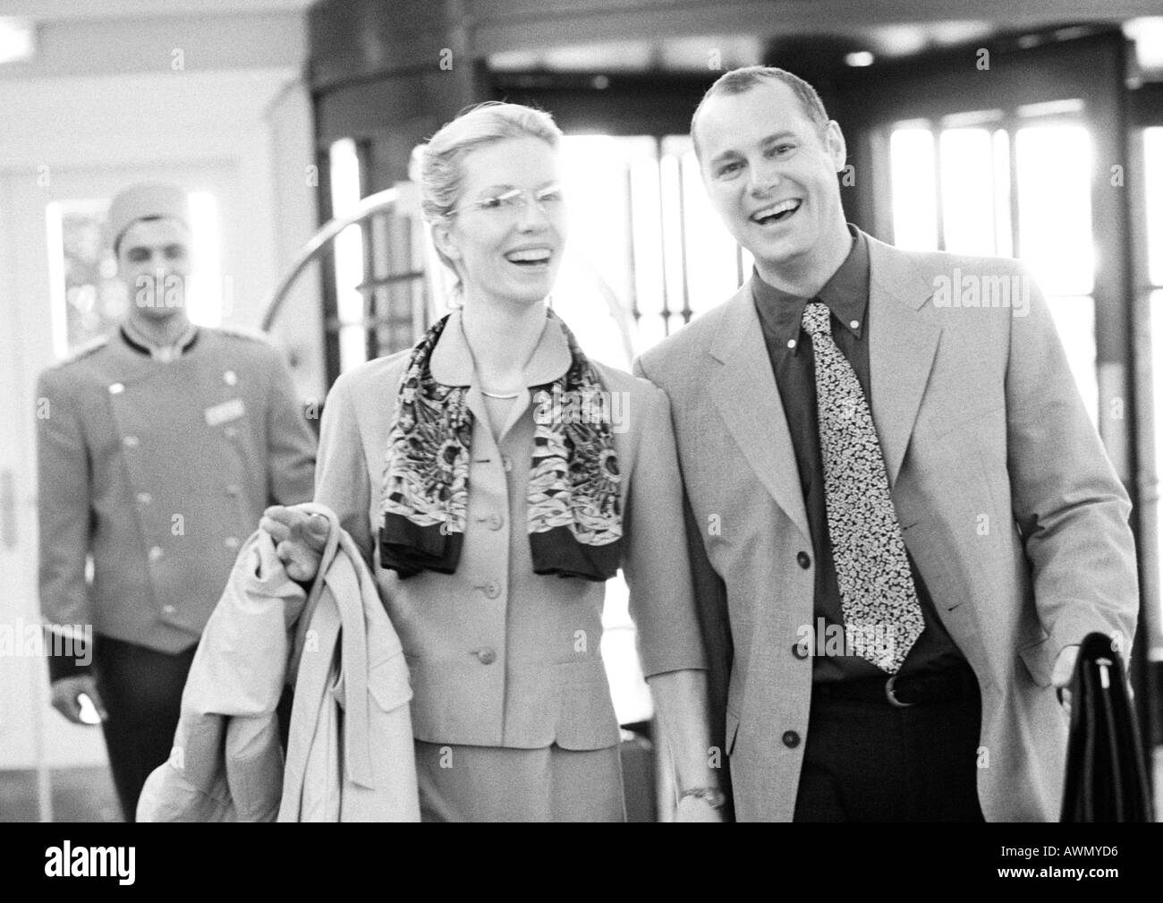 Kaufmann und Kauffrau im Hotel vor Hotelpage, lächelnd in die Kamera, b&w. Stockfoto