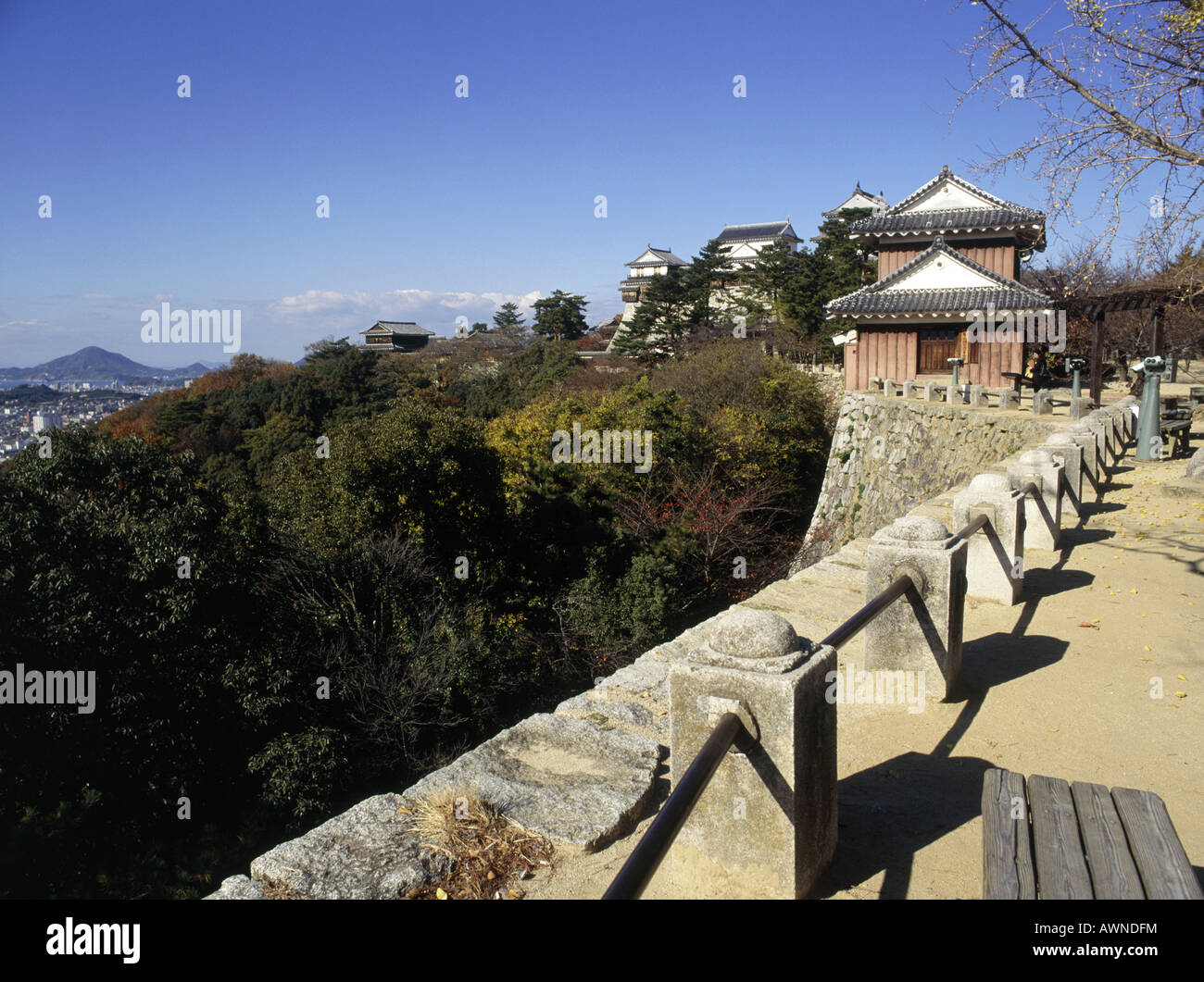 Matsuyama Schloss. Verzierte Dächer. Wände aus Stein. Geländer. Grüne Bäume. Hügel in der Ferne. Stockfoto