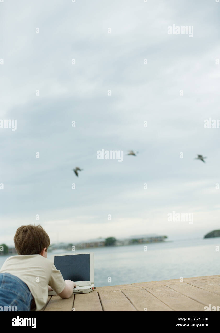 Kind am dock mit Laptop, Vögel fliegen über Wasser im Hintergrund Stockfoto