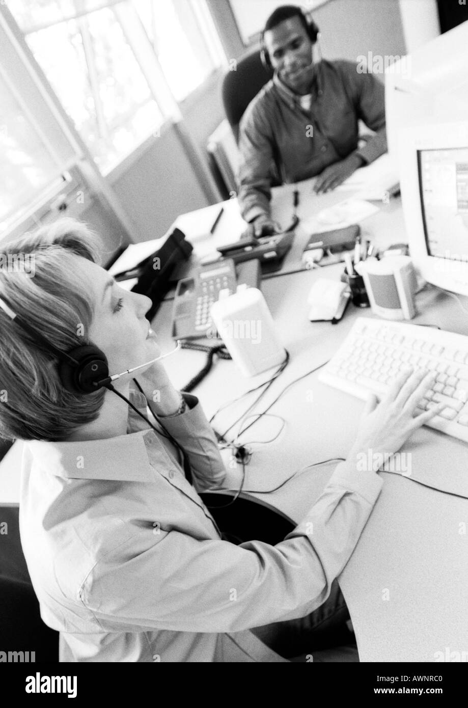Geschäftsfrau und Kollegen tragen Kopfhörer, B&W Stockfoto