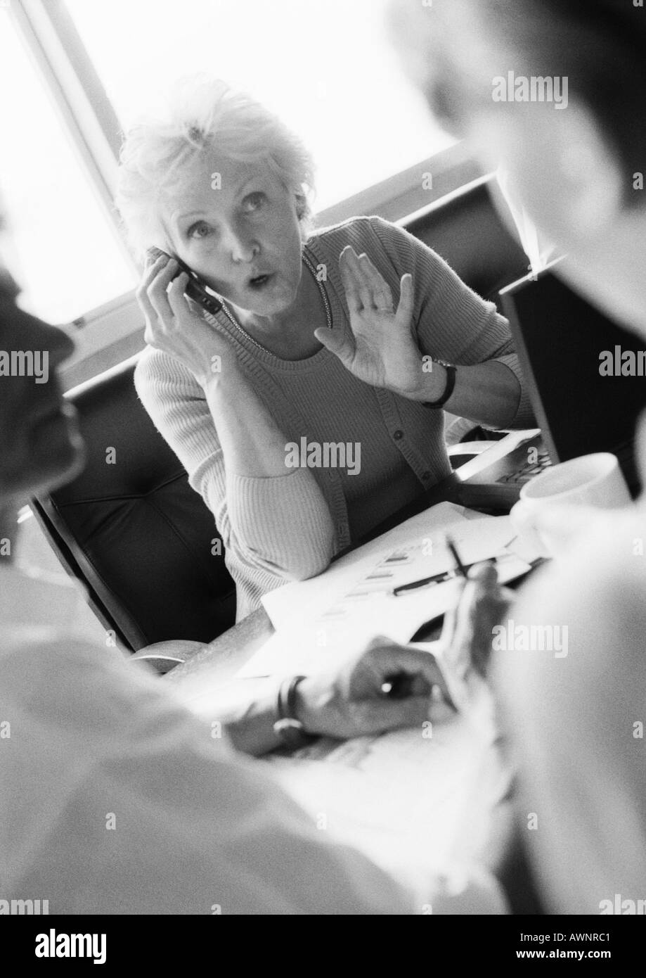 Reife Geschäftsfrau mit Handy, Kolleginnen und Kollegen im unscharfen Vordergrund, B&W Stockfoto