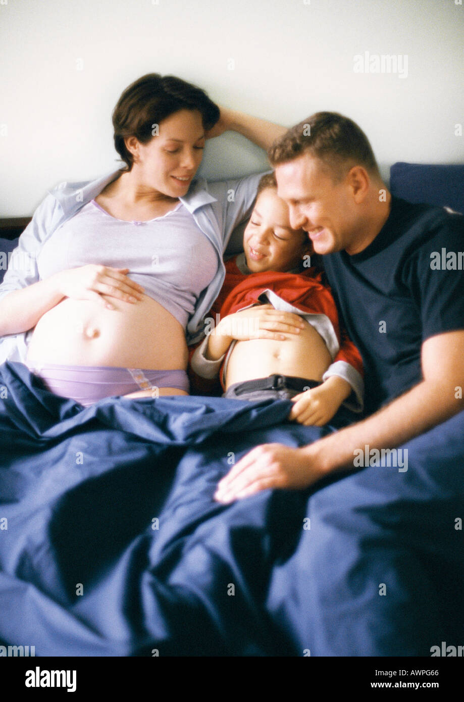 Paar und Kind zusammen im Bett, schwangere Frau und Kind zeigen Mägen Stockfoto