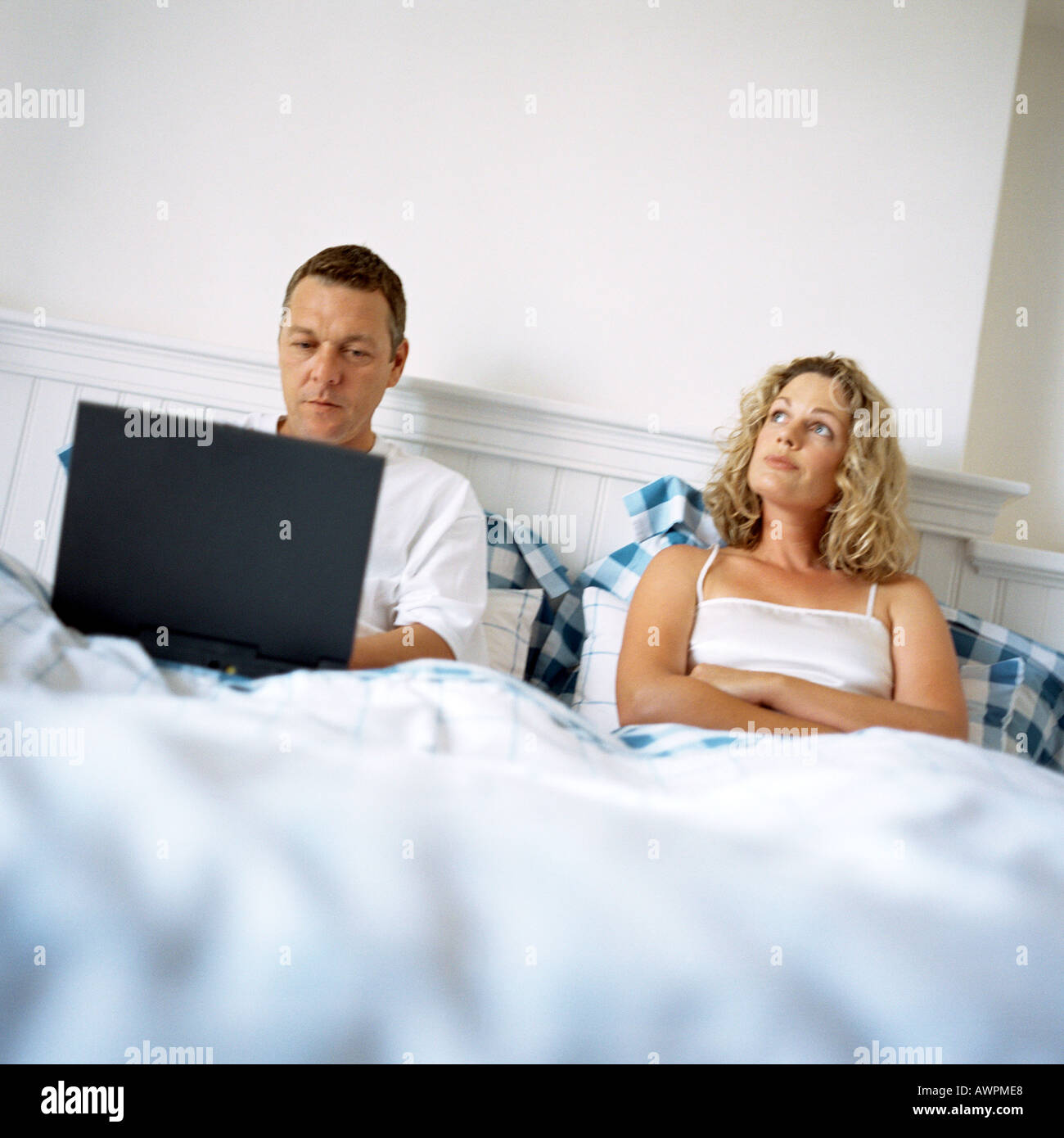 Paar im Bett, Mann mit Laptop-Computer, Frau mit verschränkten Armen Stockfoto