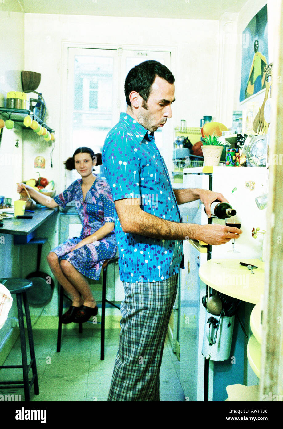 Paar in der Küche, Frau sitzt, man gießt Wein. Stockfoto