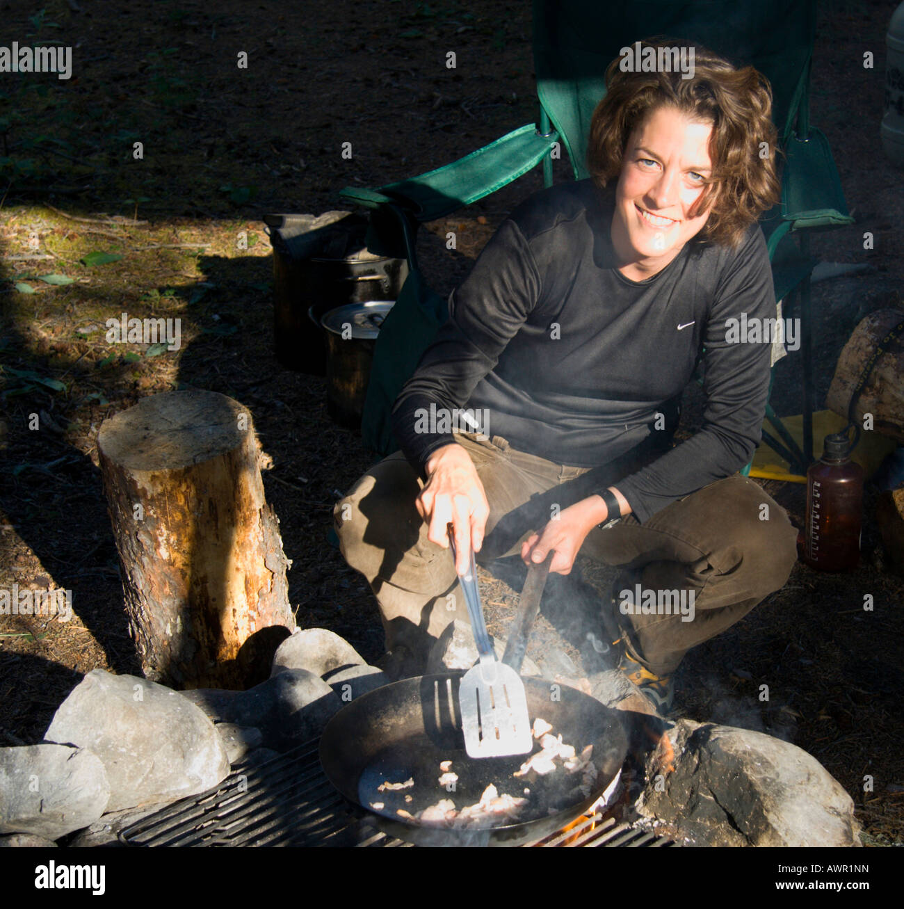 Junge Frau lächelt, Braten Speck über Lagerfeuer, Yukon Territorium, Kanada Stockfoto