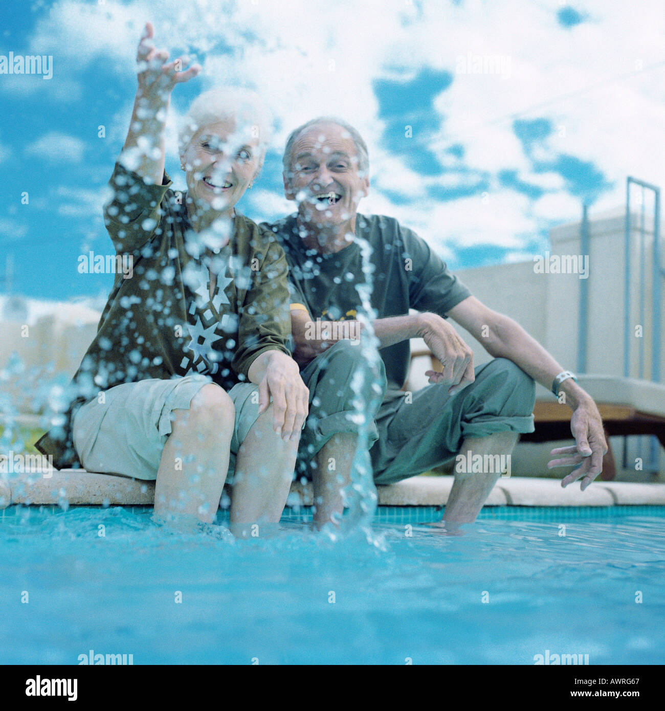 Älteres Paar sitzt am Rand des Schwimmbads Frau Spritzwasser in Luft Stockfoto