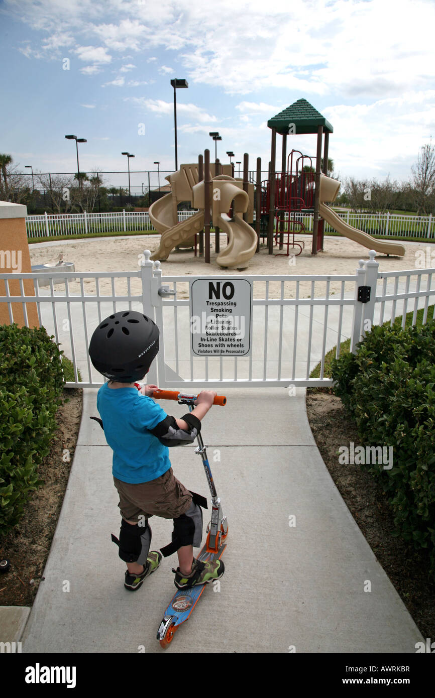 Junge mit Roller starrte auf Spielplatz Regeln Zeichen Stockfoto
