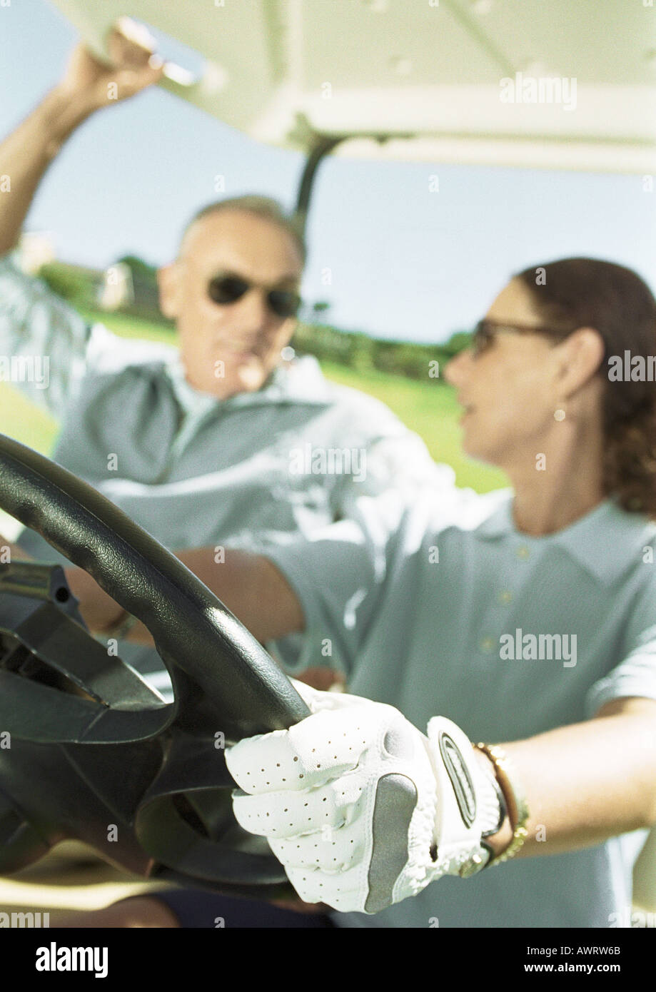 Mann und Frau im Golf-Cart, Nahaufnahme, Fokus auf Seite Reifen und Lenkrad im Vordergrund Stockfoto