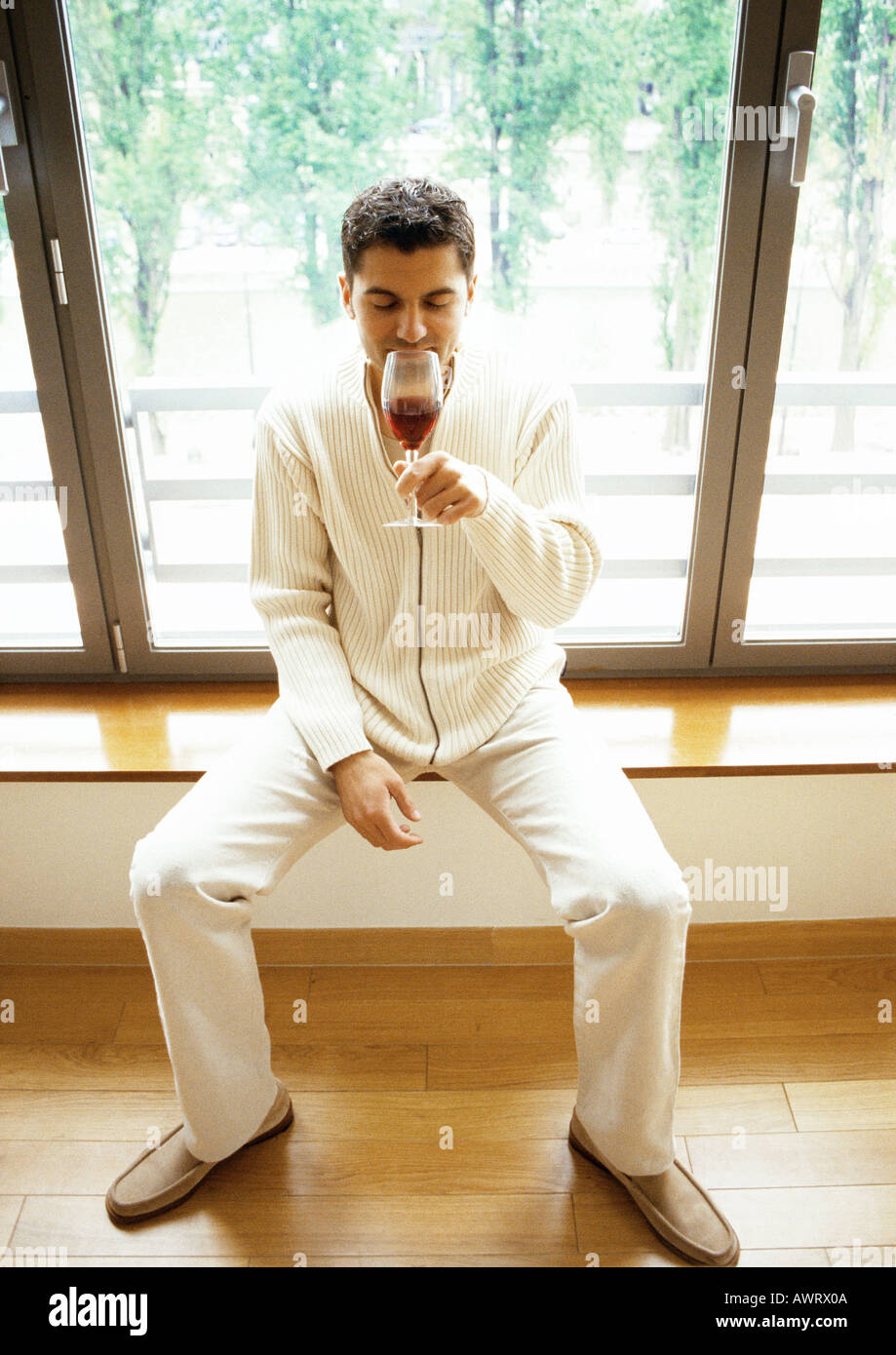 Mann sitzt vor Fenster, Wein zu trinken Stockfoto