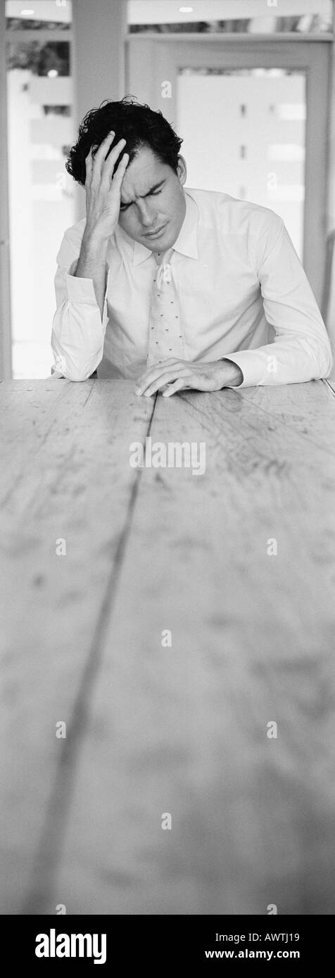 Mann sitzt am Ende der Tabelle hielt Kopf mit Hand, b&w, vertikale Stockfoto