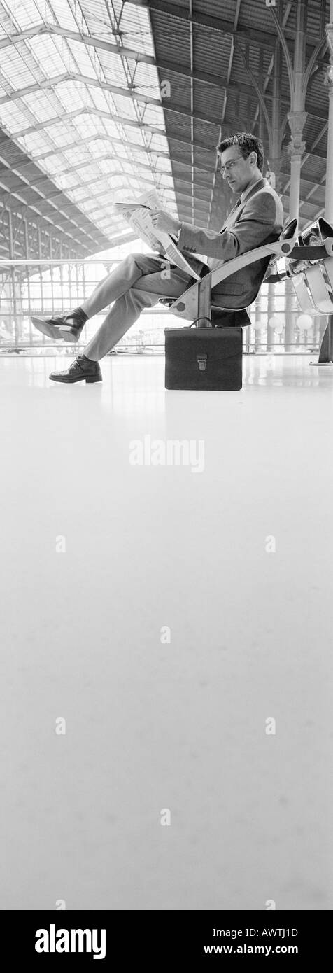 Mann sitzt im Bahnhof, lesen Zeitung, b&w, vertikale Stockfoto