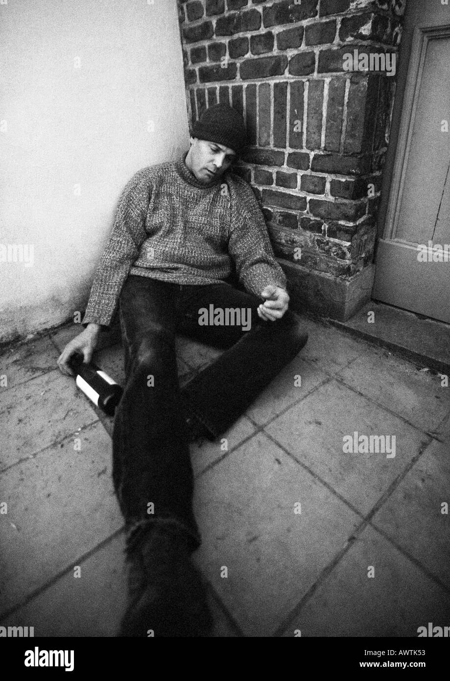 Mann sitzt auf Boden mit Flasche in der hand und geschlossenen Augen Stockfoto