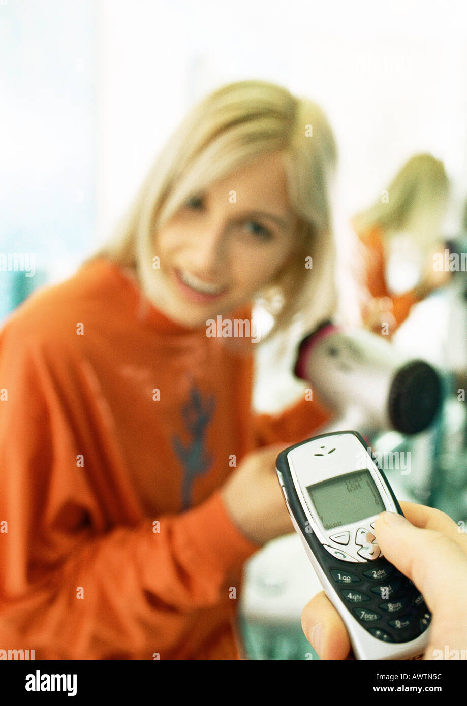 Mannes Hand mit Handy, Frau föhnen Haare im Hintergrund Stockfoto